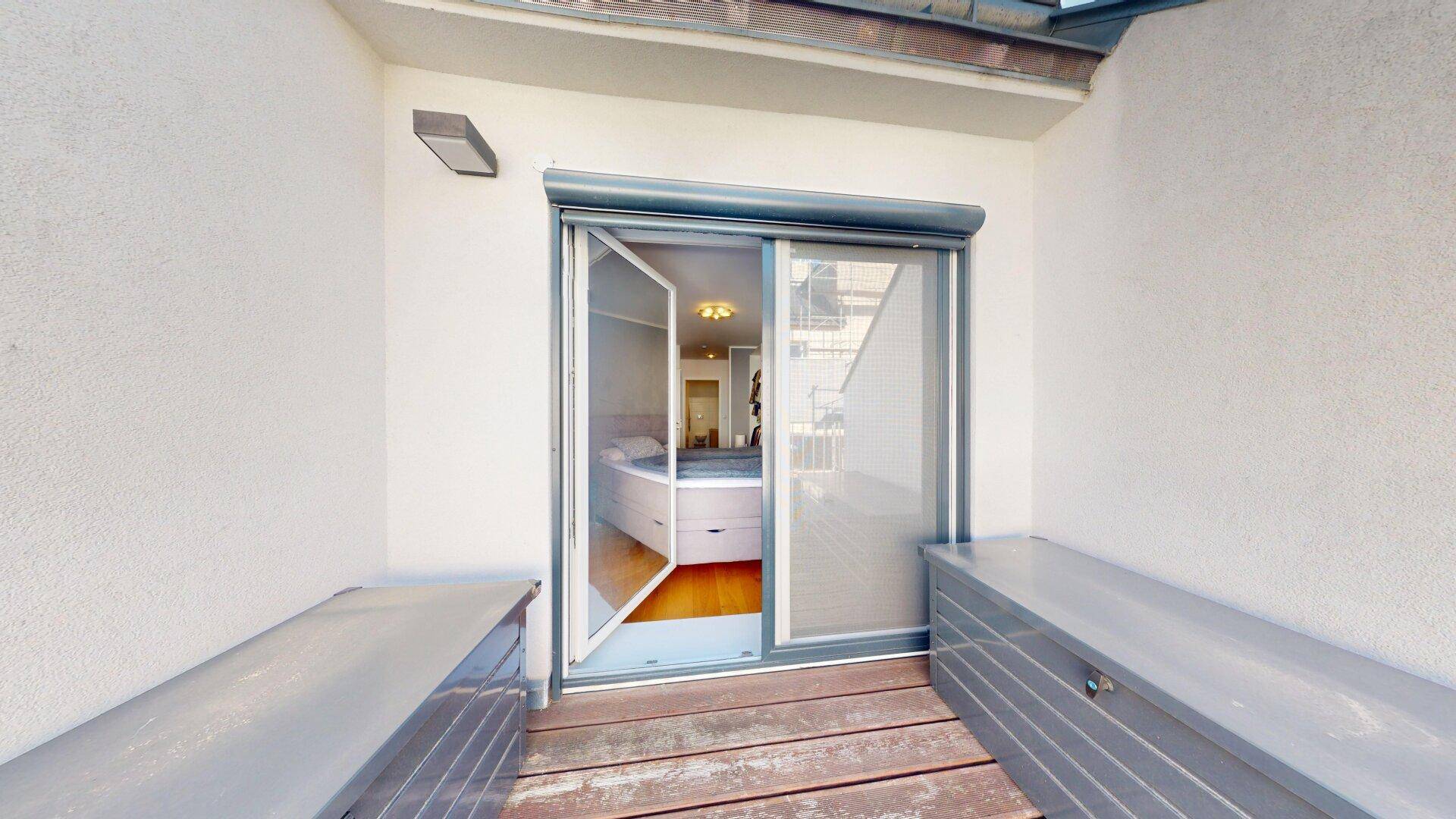 Balkon mit Holzboden und Zugang zum Schlafzimmer, ausgestattet mit Rollläden.