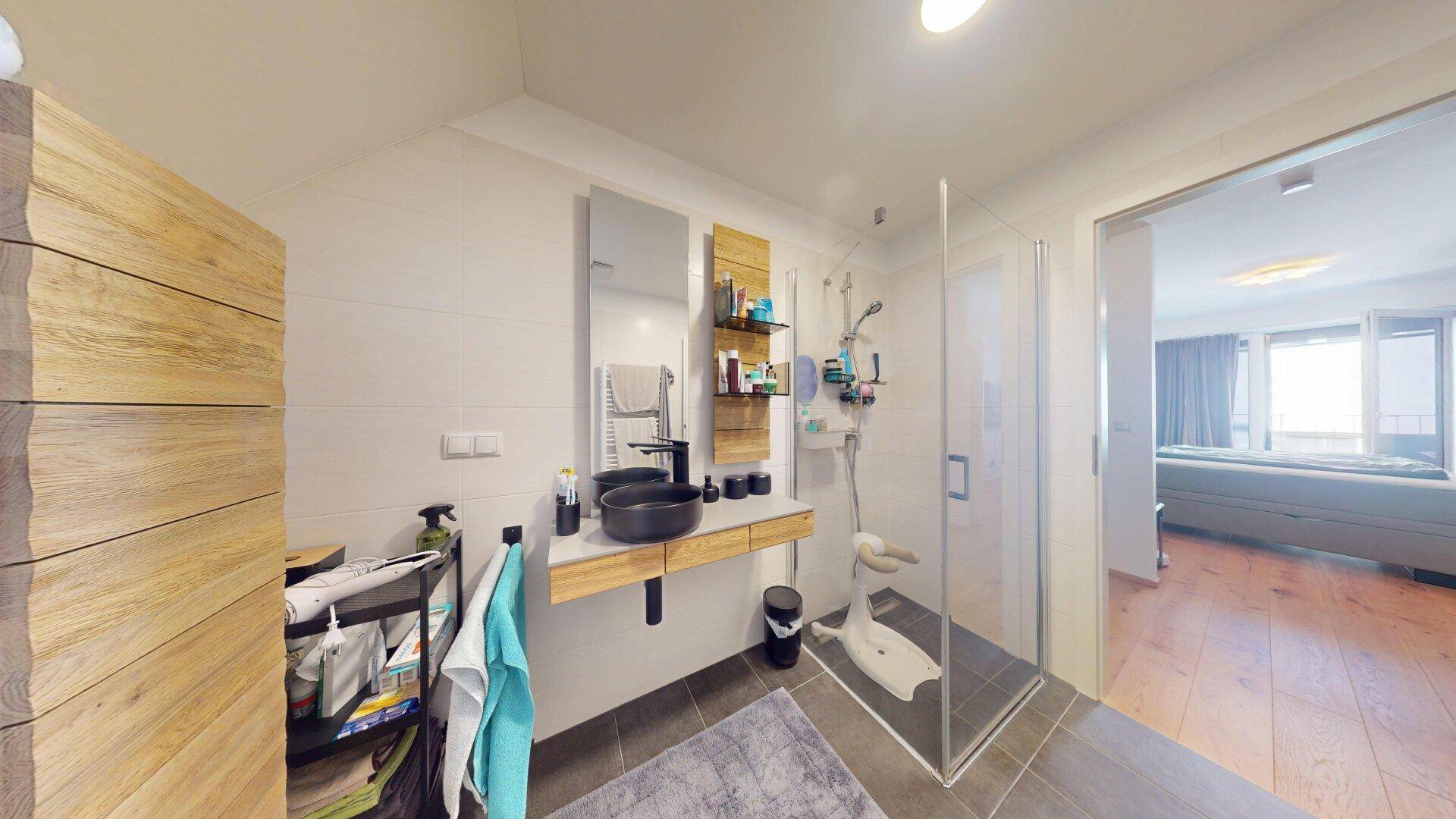 Helles Badezimmer mit großer Dusche, modernem Waschbecken und Zugang zum Schlafzimmer.