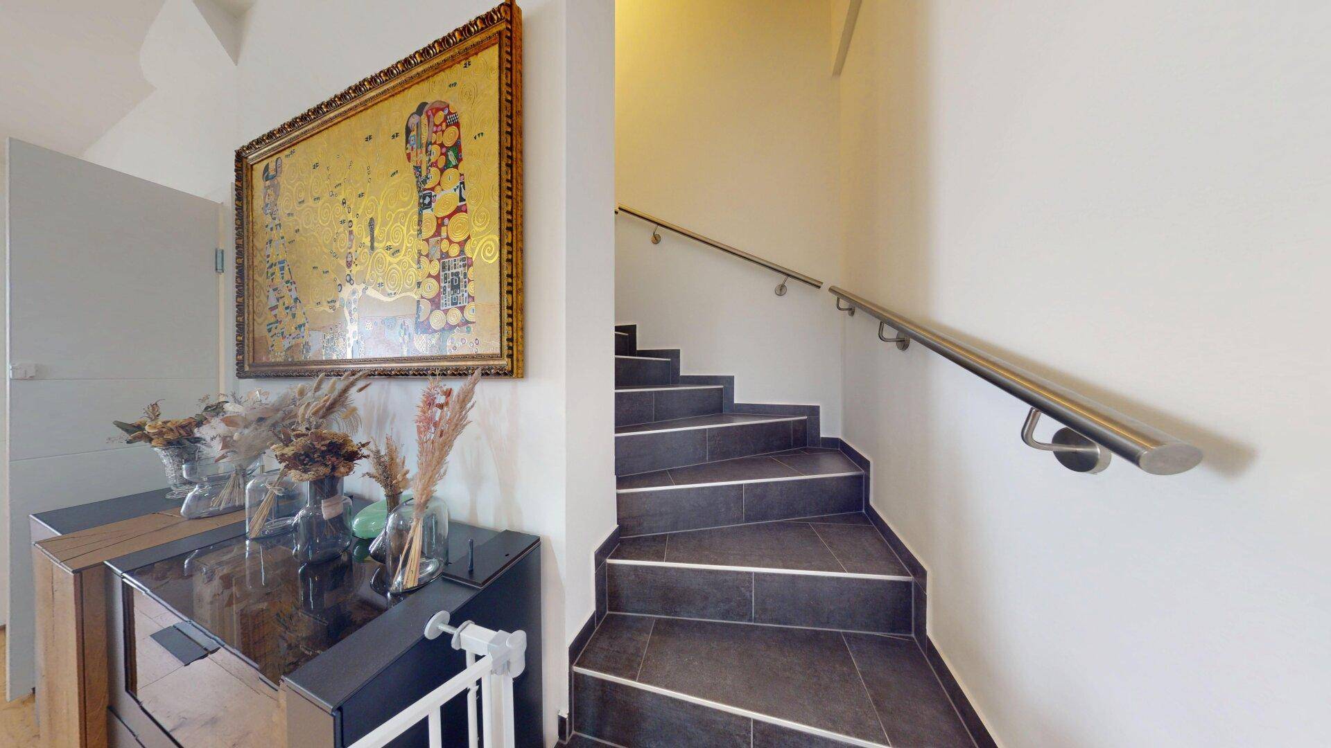 Treppenhaus mit gefliesten Stufen, Edelstahlhandlauf und Kunstwerk an der Wand.
