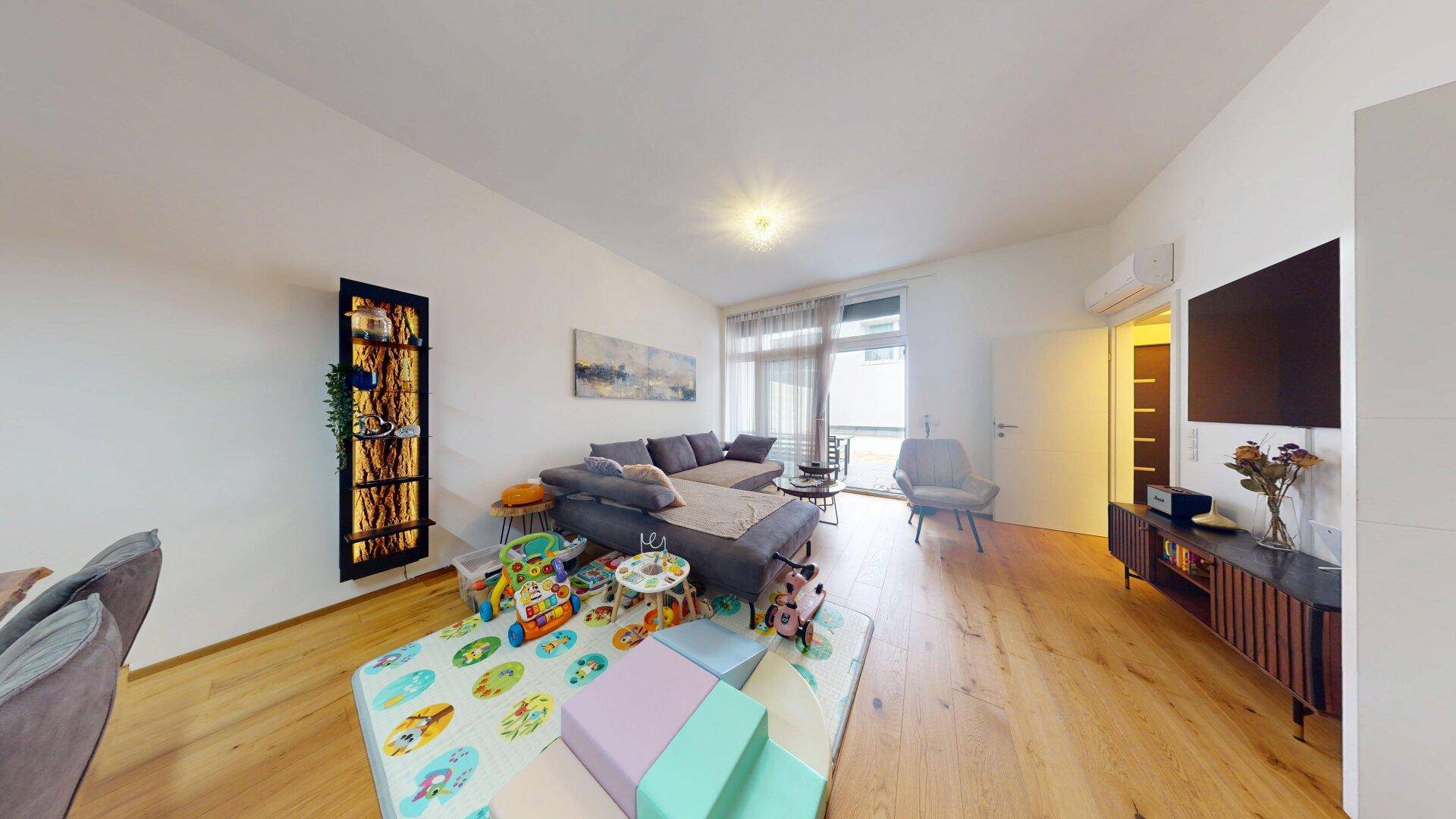 Gemütliches Wohnzimmer mit großem Sofa, Holzboden und Zugang zu einem Balkon, ideal für Familien.