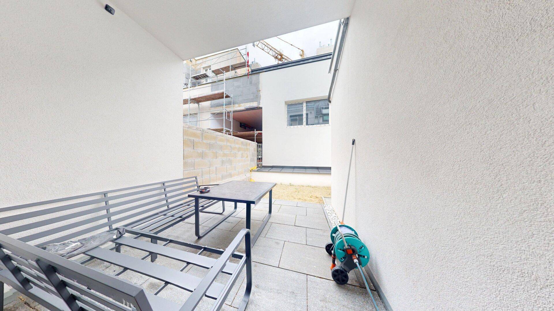 Teilweise überdachte Terrasse mit Sitzgelegenheiten und Blick auf die Baustelle des Nachbargebäudes.