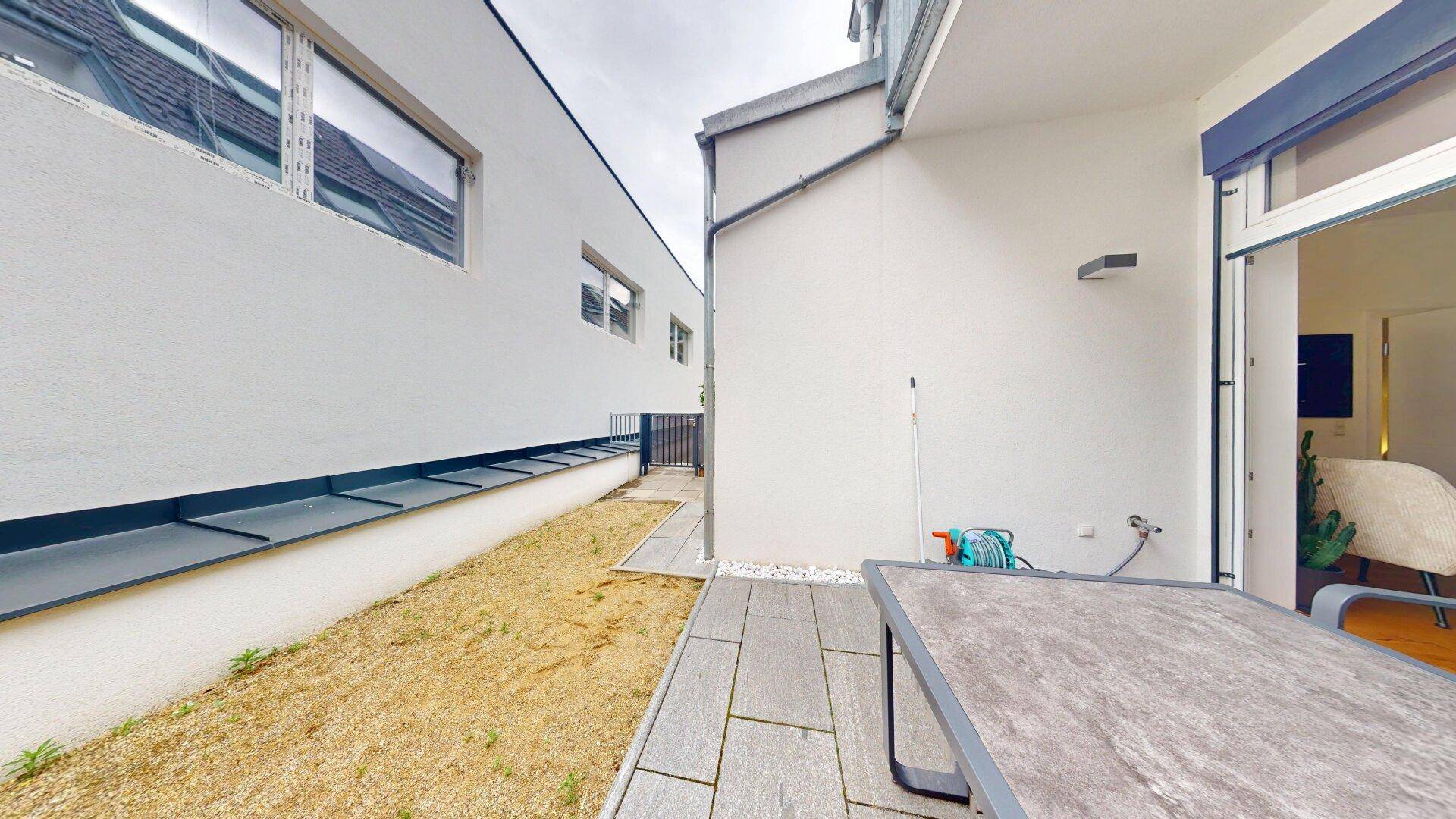 Außenbereich mit gepflasterter Terrasse und einem kleinen, noch unfertigen Gartenstreifen neben dem Gebäude.