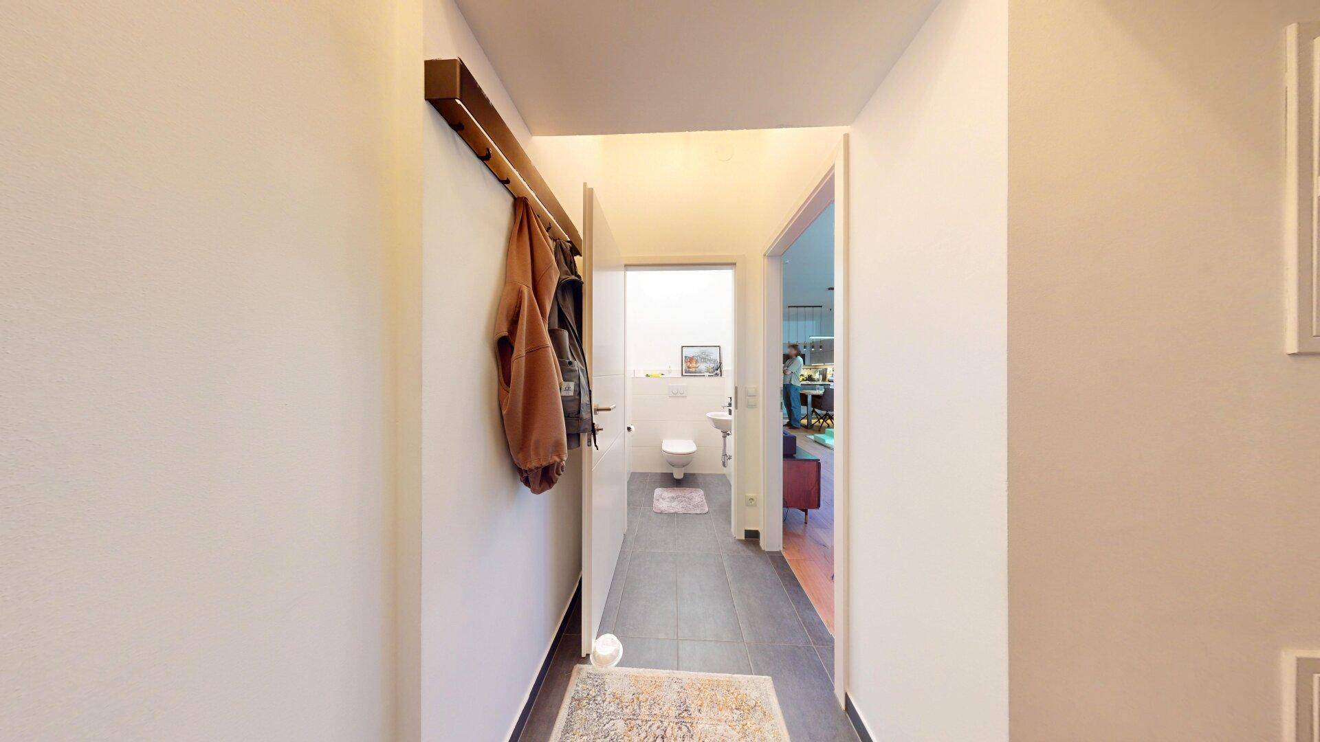 Heller Flur mit Fliesenboden und Garderobe, der zu einem Gäste-WC und weiteren Räumen führt.
