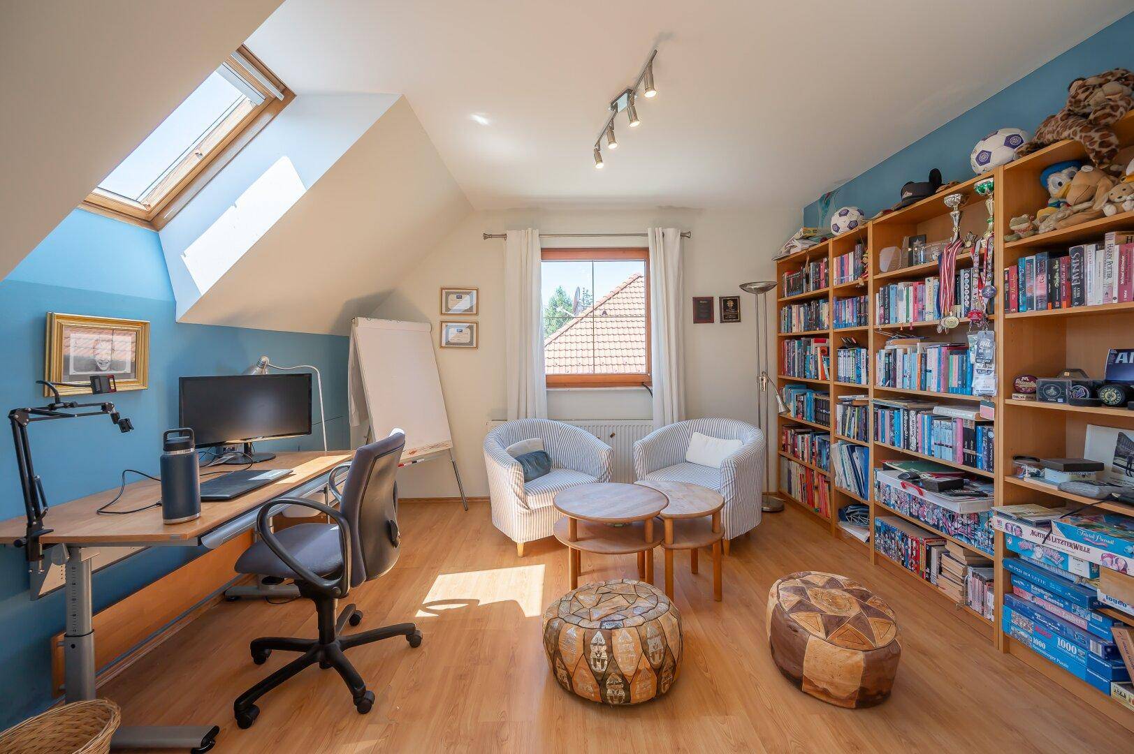 Helles Arbeitszimmer im Dachgeschoss mit Dachfenstern, Bücherregalen und einem Schreibtischbereich.