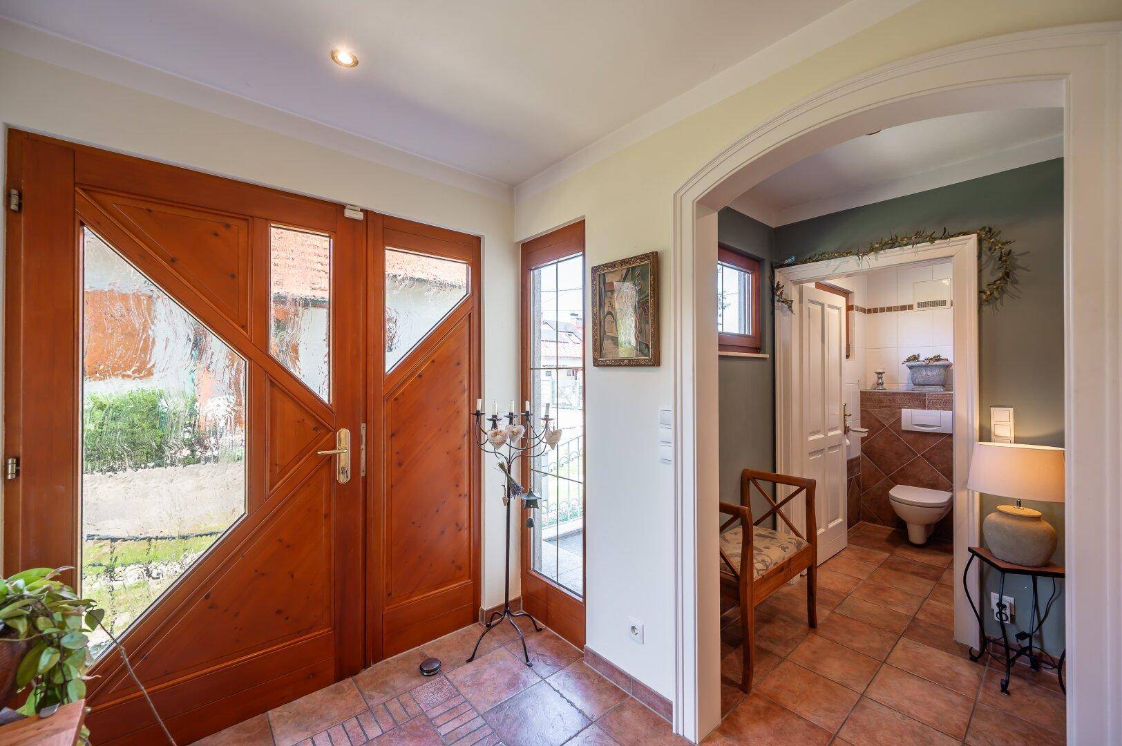 Heller Eingangsbereich mit Holztüren und Blick in ein Badezimmer mit Toilette und Fliesenboden.