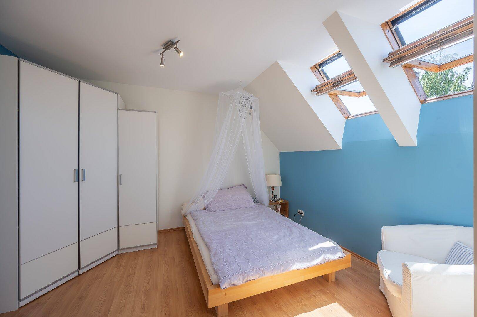 Schlafzimmer im Dachgeschoss mit Dachfenstern, Einzelbett und weißen Kleiderschränken, hell und freundlich.
