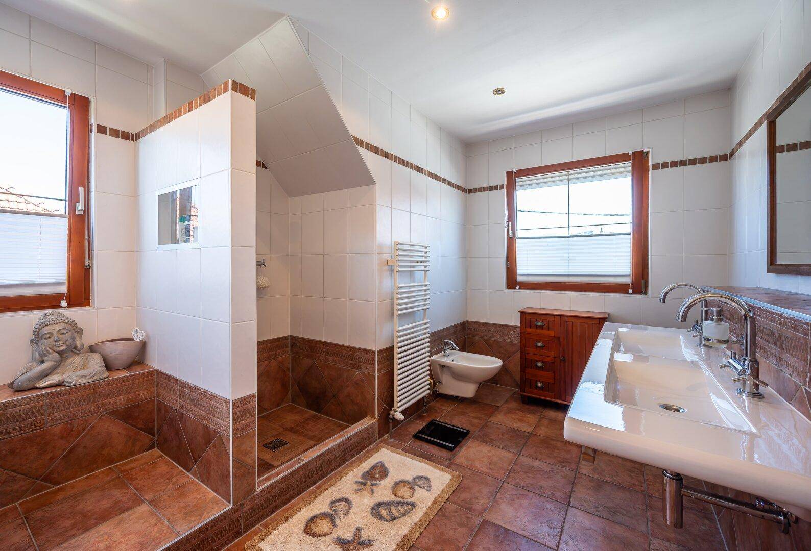 Geräumiges Badezimmer mit großer begehbarer Dusche, Doppelwaschbecken, Bidet und Handtuchheizkörper.