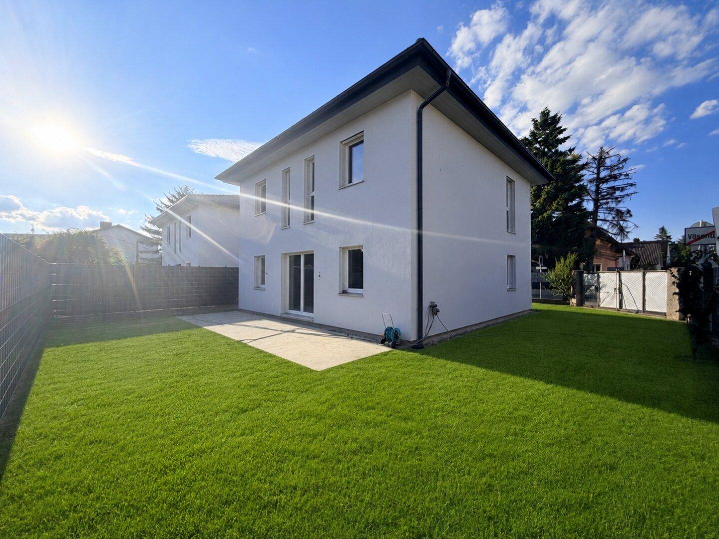 Rückseite eines modernen Hauses mit großer Rasenfläche und sonniger Terrasse.