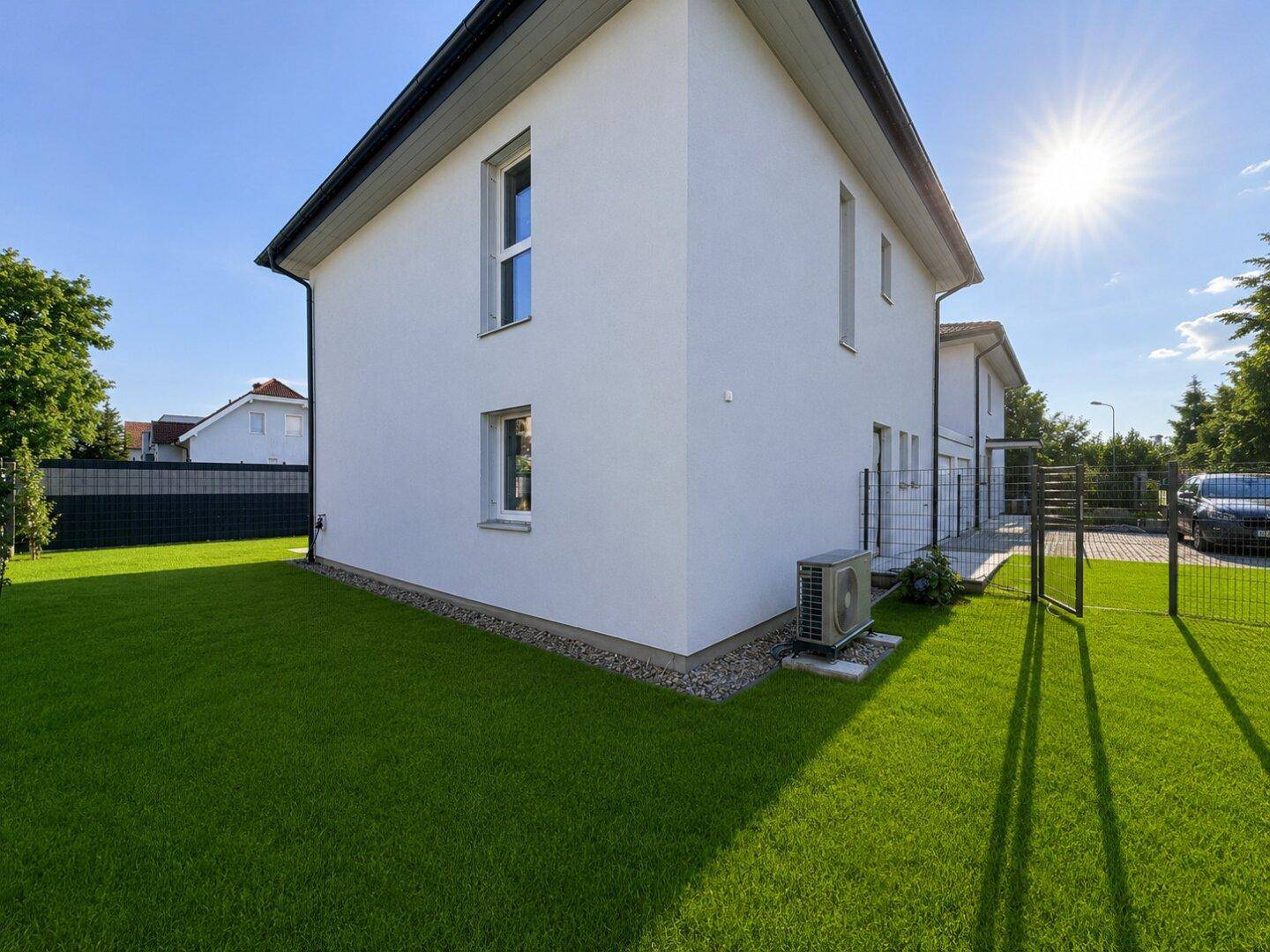 Seitenansicht des Hauses mit grüner Rasenfläche und einer Außeneinheit für die Klimaanlage.