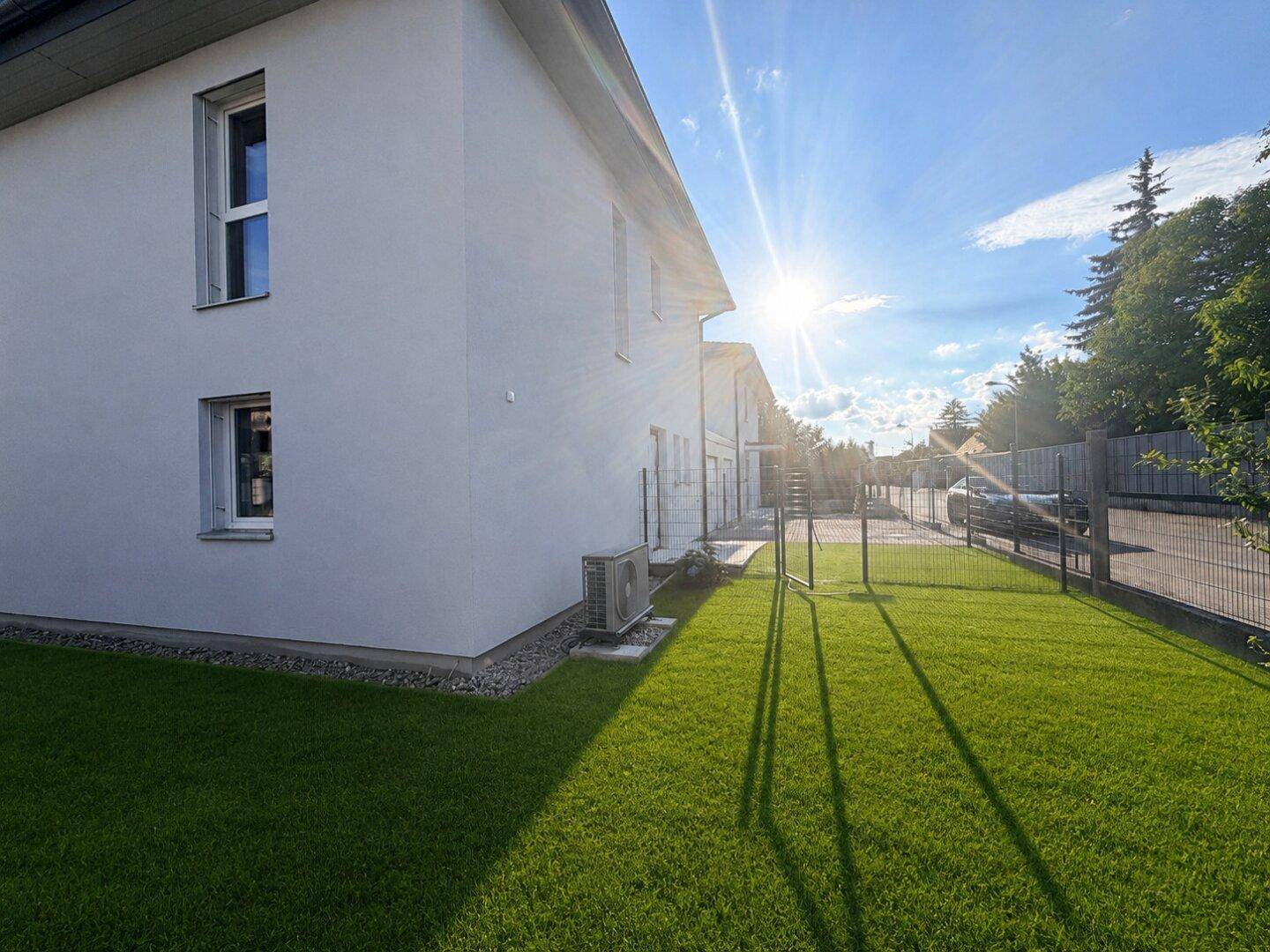 Sonnige Seitenansicht des Hauses mit gepflegtem Rasen und einer Außeneinheit für die Klimaanlage.