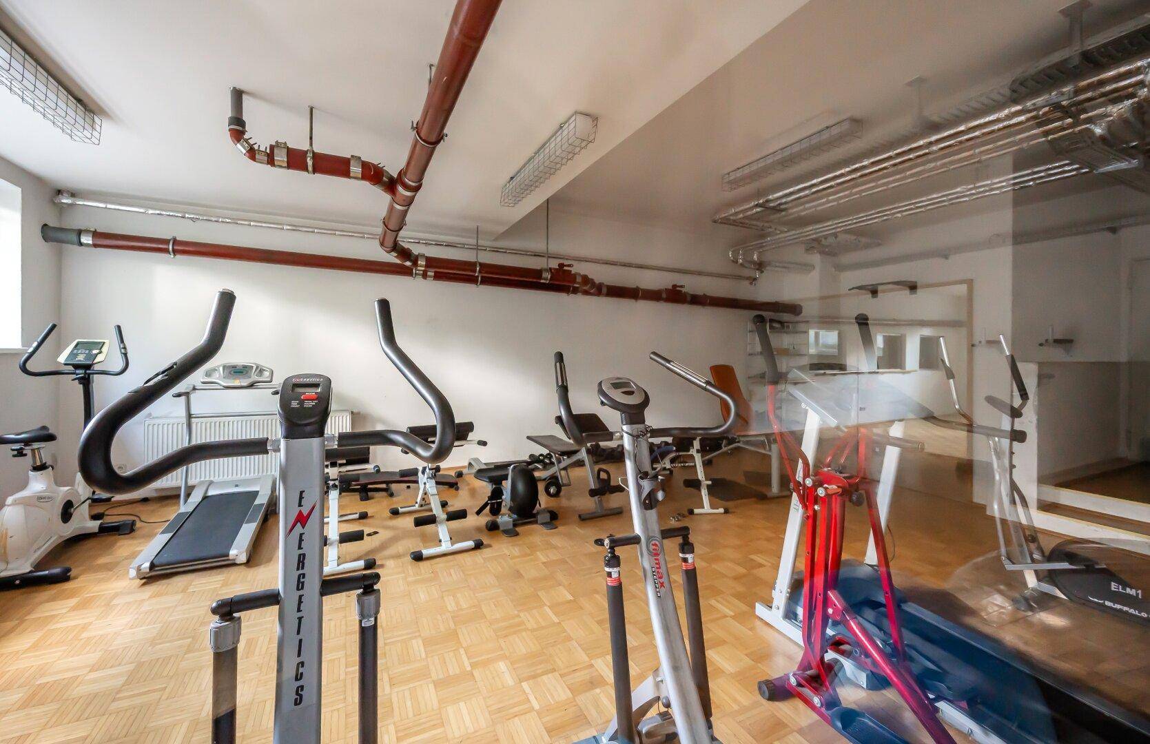 Gemeinschaftlicher Fitnessraum mit verschiedenen Trainingsgeräten und Parkettboden.