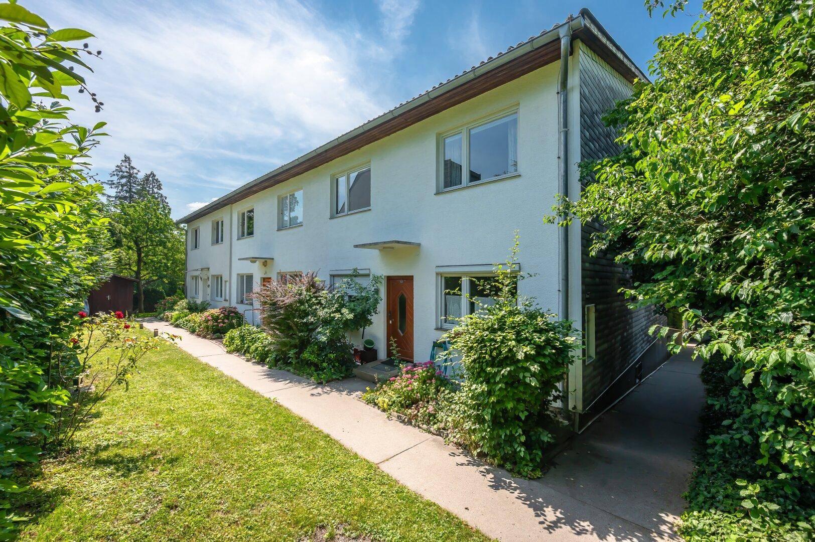 Mehrfamilienhaus mit weißer Fassade, umgeben von gepflegtem Grün und Bäumen.