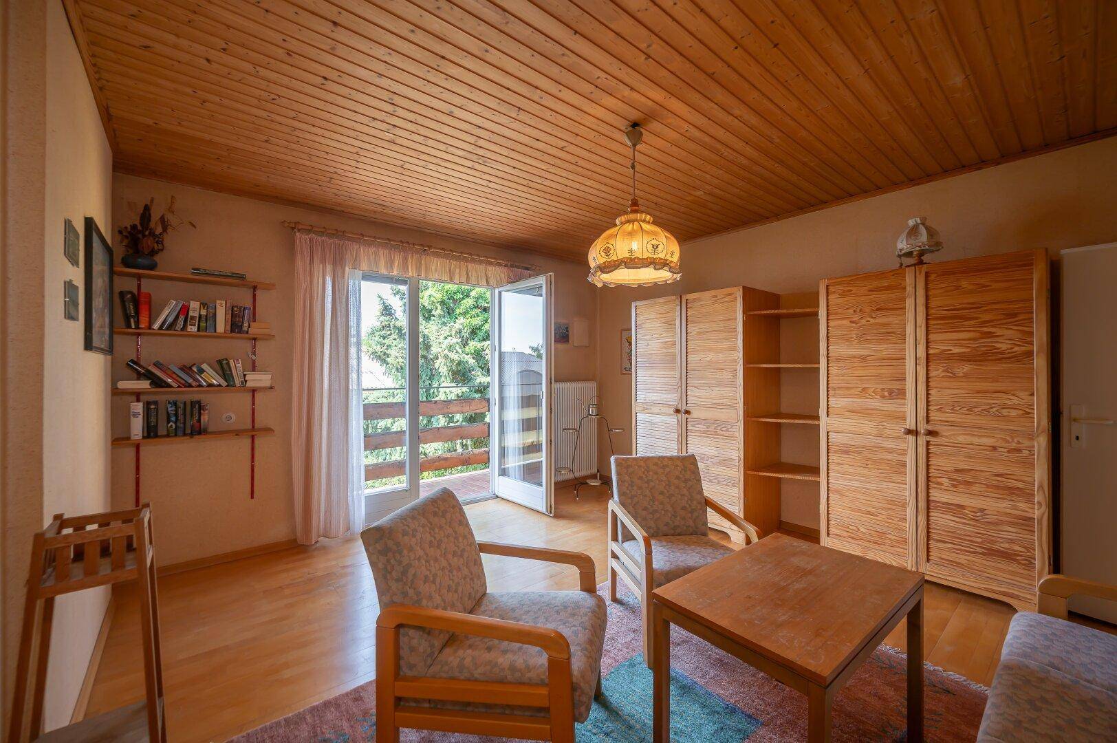 Gemütliches Wohnzimmer mit Holzdecke, Parkettboden und Zugang zu einem Balkon.