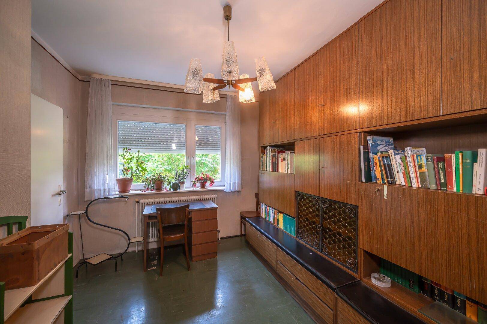 Arbeitszimmer mit Holzvertäfelung, integrierten Regalen und Blick auf den Garten.