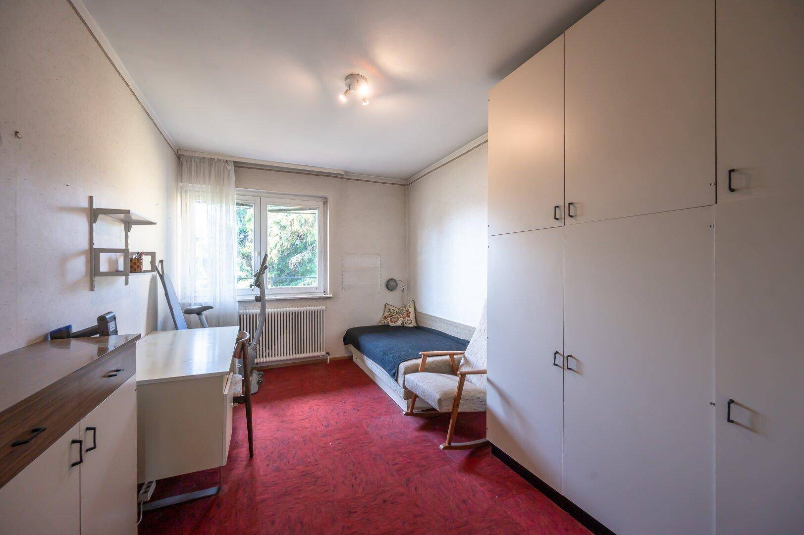 Schlafzimmer mit rotem Teppichboden, Einzelbett und weißem Kleiderschrank.