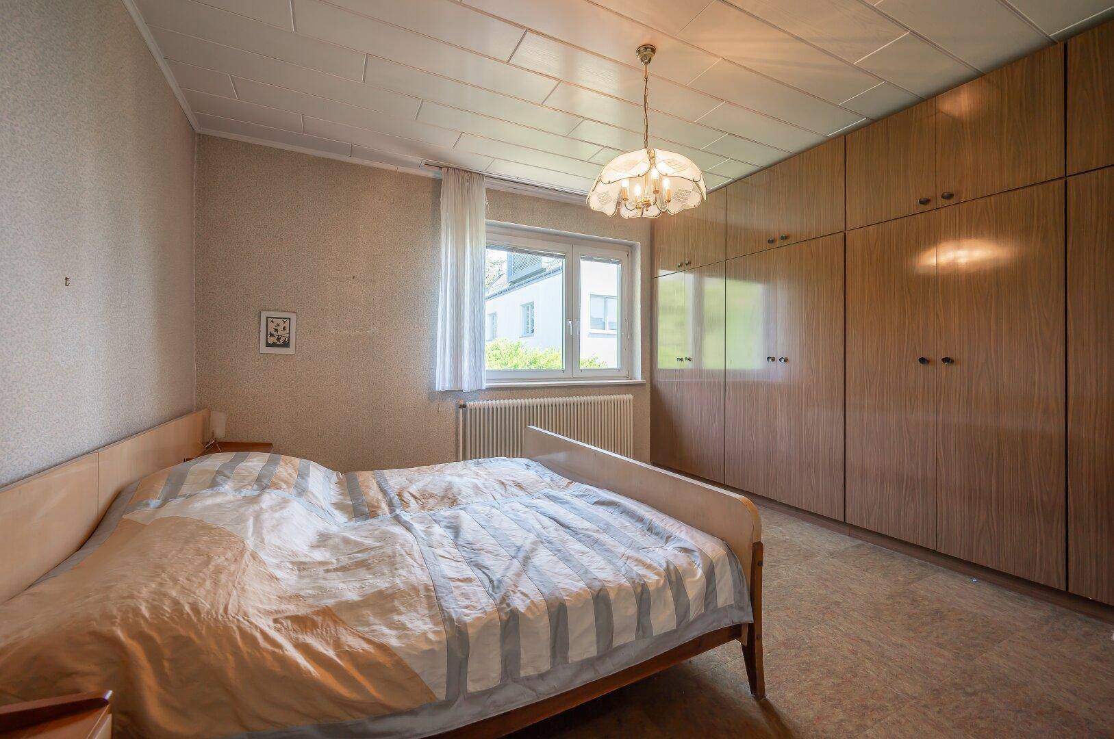 Schlafzimmer mit Doppelbett, Holzschränken und Fenster mit Blick ins Grüne.