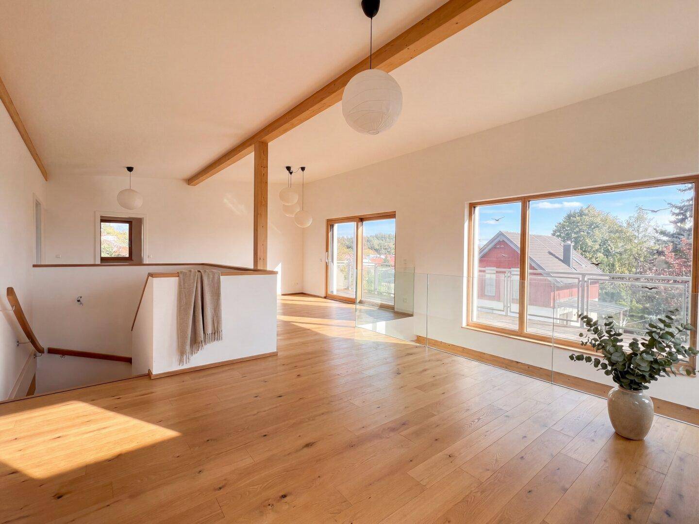 Heller Flurbereich im Obergeschoss mit Holzboden, großen Fenstern und Zugang zu einem Balkon.