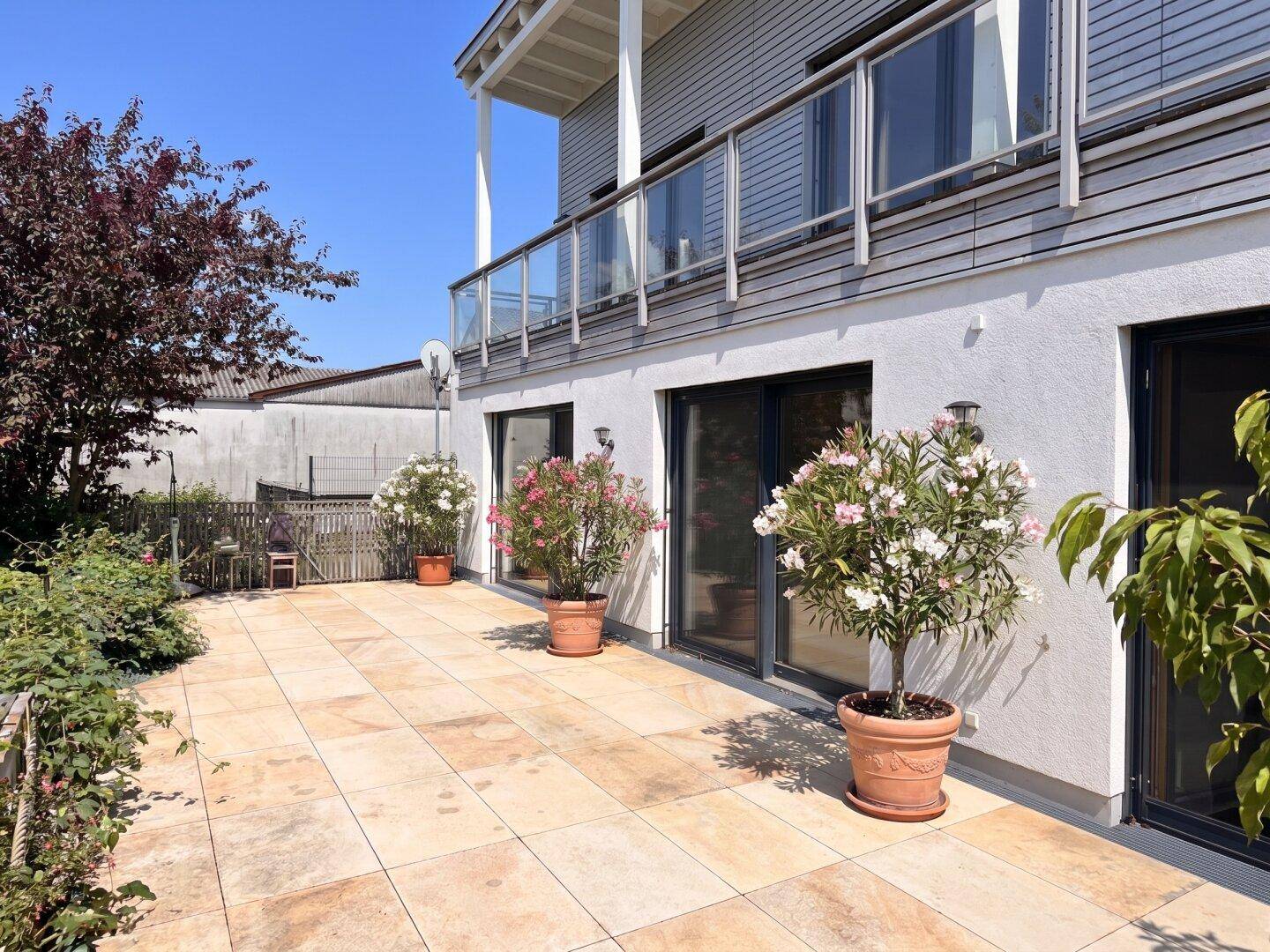 Große geflieste Terrasse mit Pflanzenkübeln und Zugang zum Haus, sonnig und gepflegt.