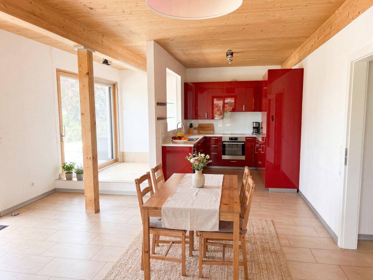 Moderne, offene Küche in Rot mit Essbereich und Holzbalkendecke, hell und einladend.