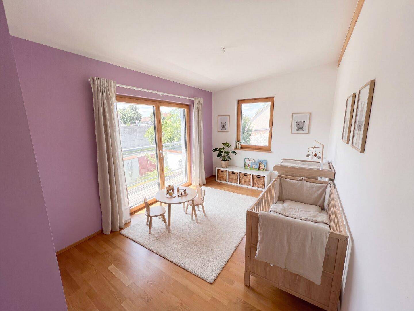 Freundliches Kinderzimmer mit lila Akzentwand, Holzboden und Zugang zu einem Balkon.