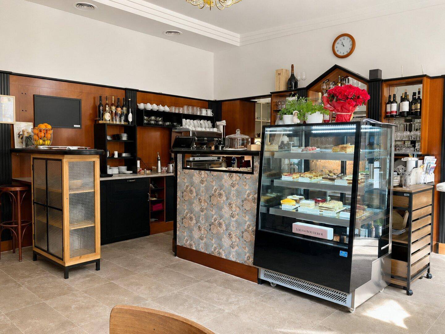 Einladender Café-Bereich mit einer Kuchenvitrine, einer Theke und Regalen voller Getränke und Geschirr.