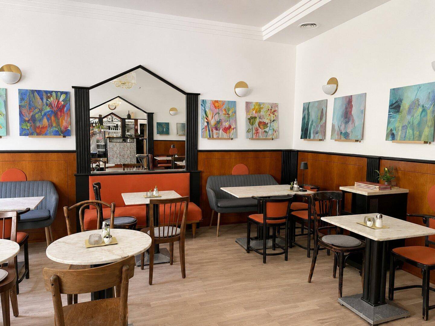 Heller Café-Essbereich mit verschiedenen Sitzgelegenheiten, Holztäfelung und farbenfrohen Kunstwerken an den Wänden.