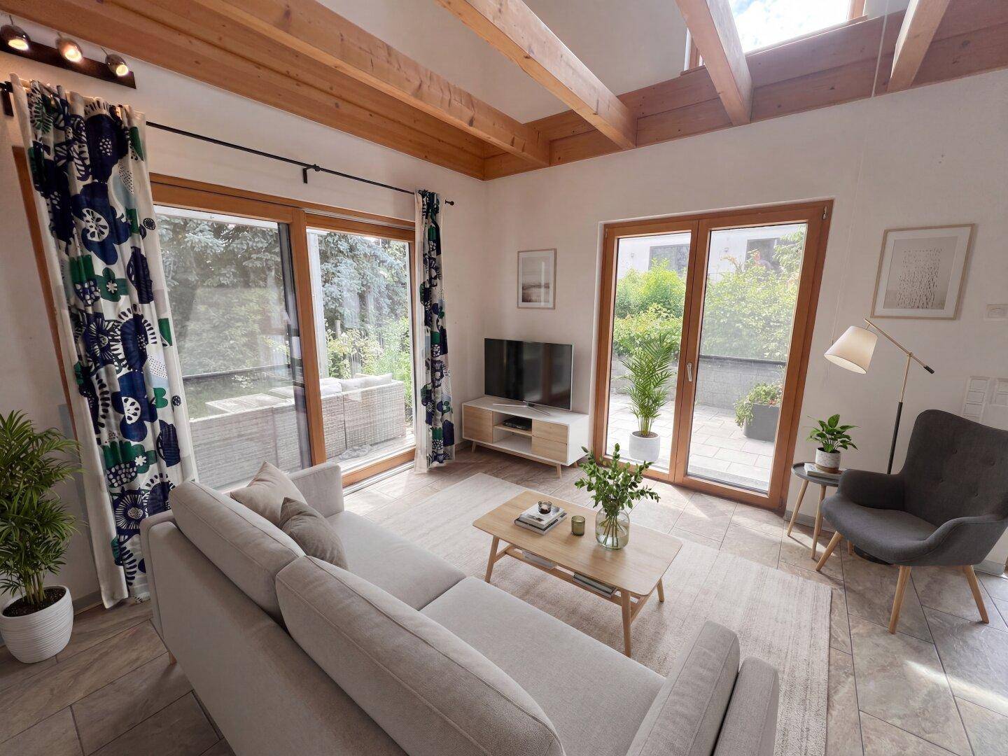 Helles Wohnzimmer mit Holzbalkendecke, großen Fenstern und Zugang zur Terrasse.