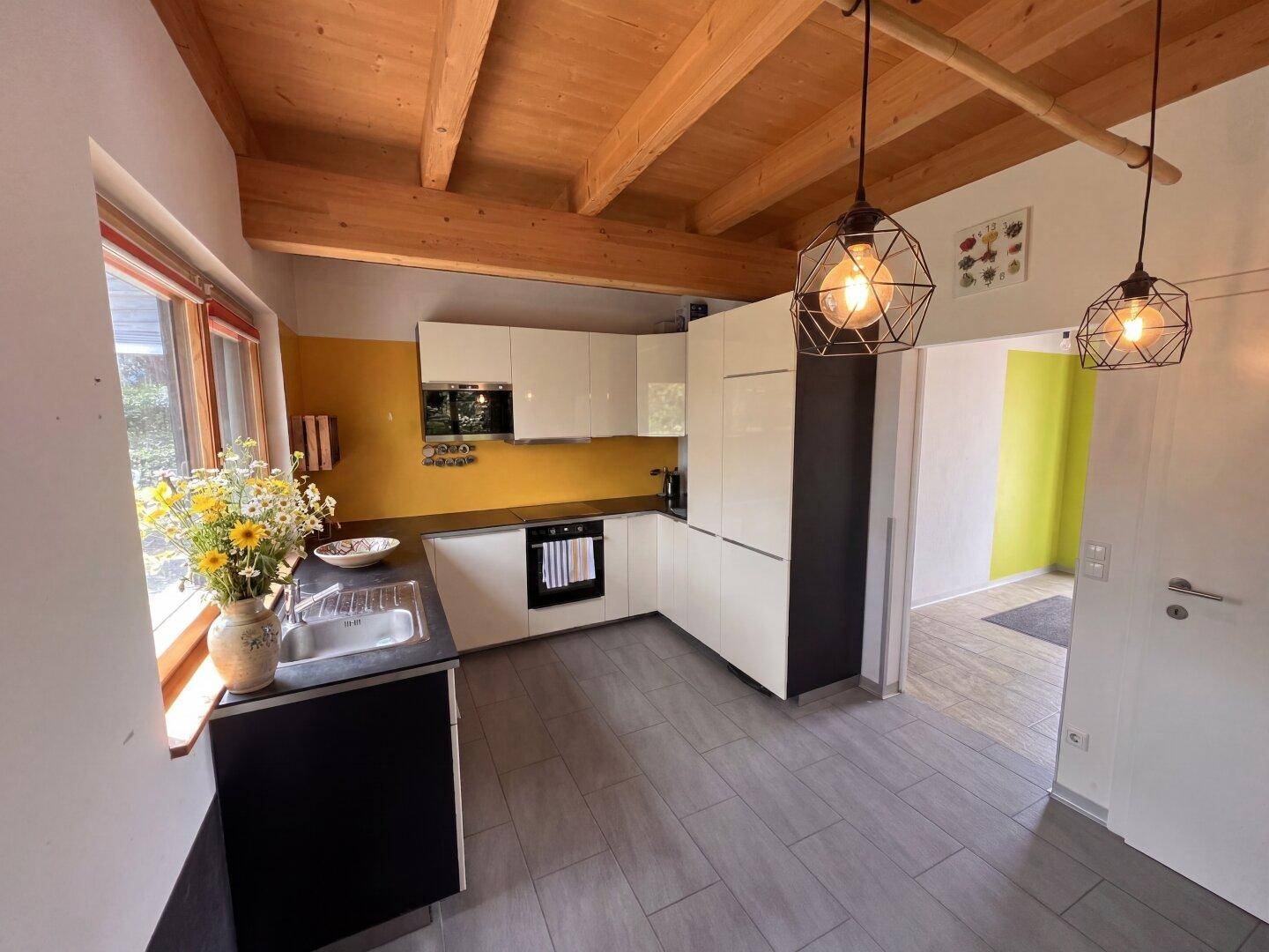 Moderne Küche mit weißen Hochglanzfronten, Holzbalkendecke und gelber Akzentwand.