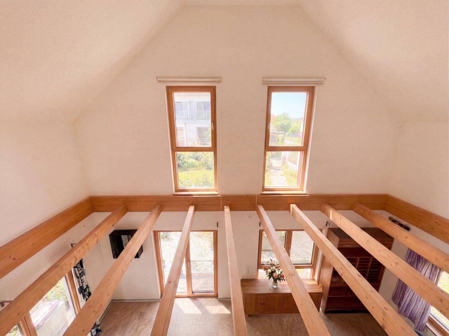 Offener Dachbodenbereich mit sichtbaren Holzbalken und hohen Fenstern, bietet viel Potenzial.
