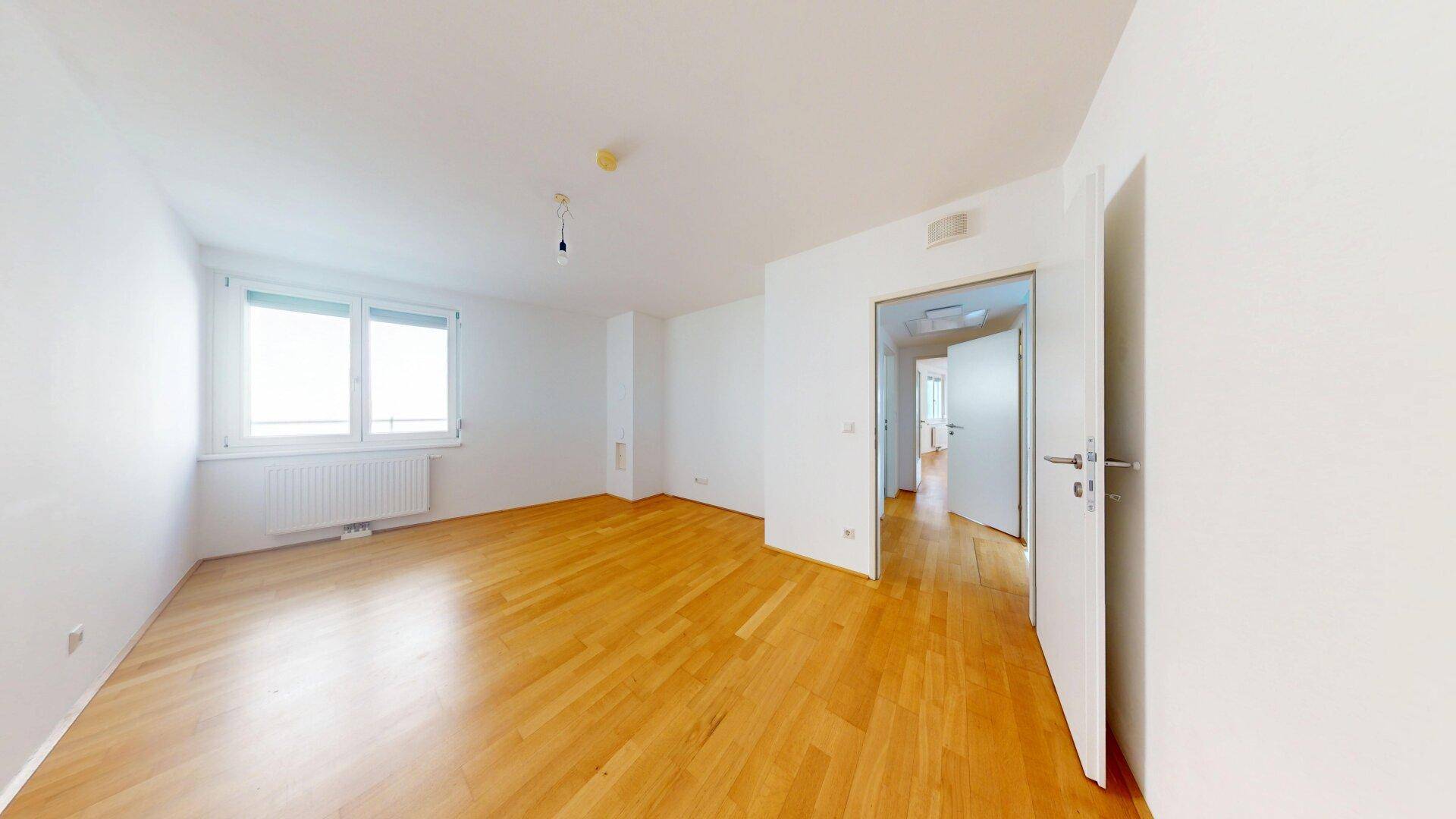 Helles Zimmer mit Parkettboden und Zugang zu einem weiteren Flur.
