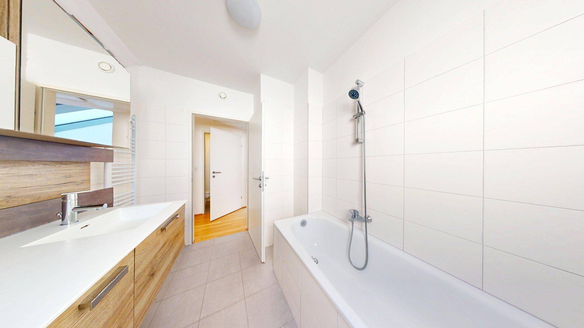 Helles Badezimmer mit Badewanne, Waschbecken und Holzmöbeln.
