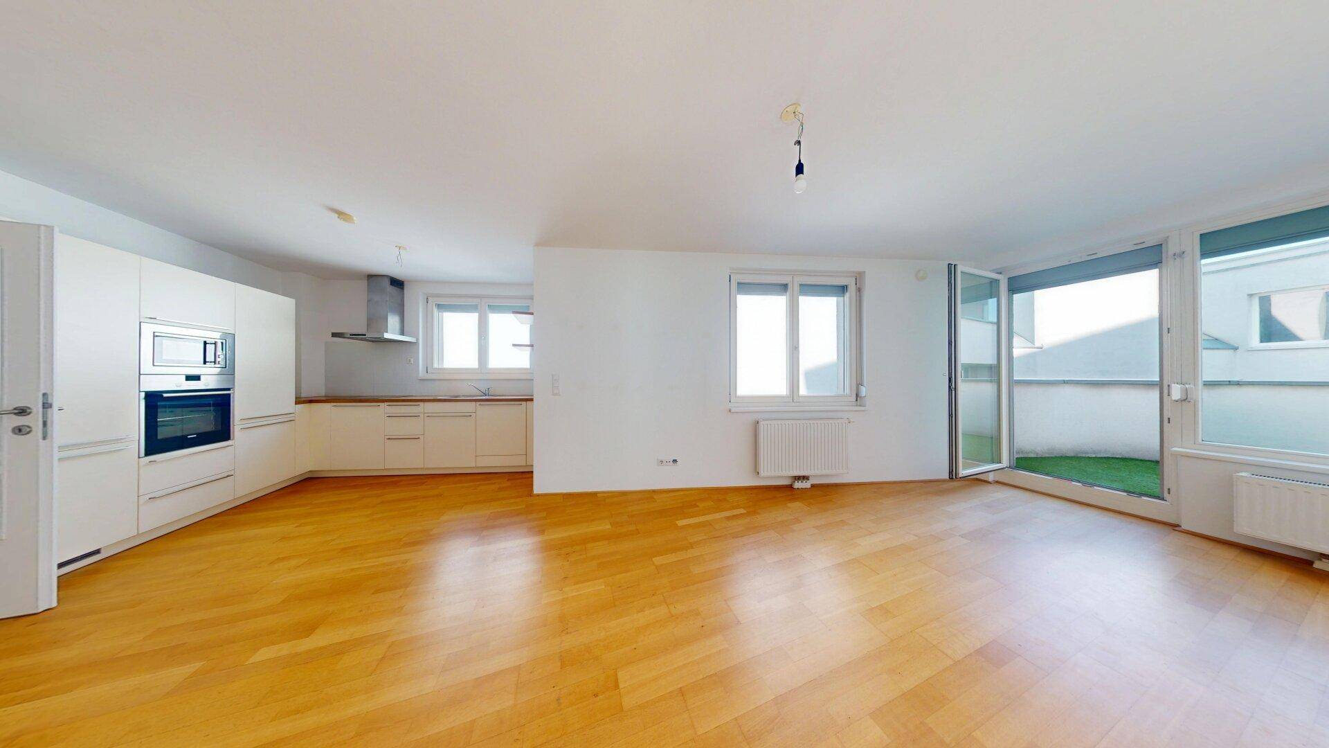 Heller offener Wohnbereich mit integrierter Küche, Parkettboden und Zugang zur Terrasse.