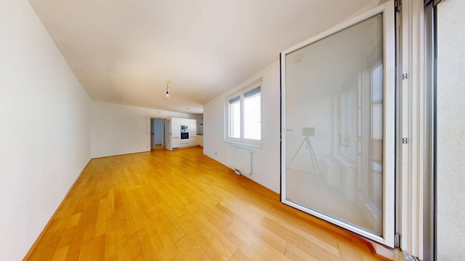 Heller Wohnbereich mit Parkettboden und großem Fenster mit Zugang nach draußen.