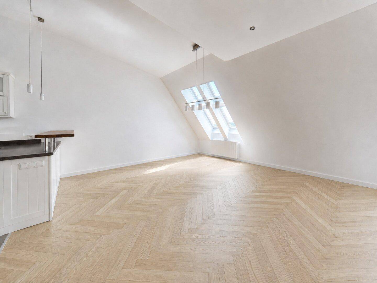 Geräumiges Dachgeschosszimmer mit schrägen Wänden, Fischgrätparkett und einem einzelnen Dachfenster.