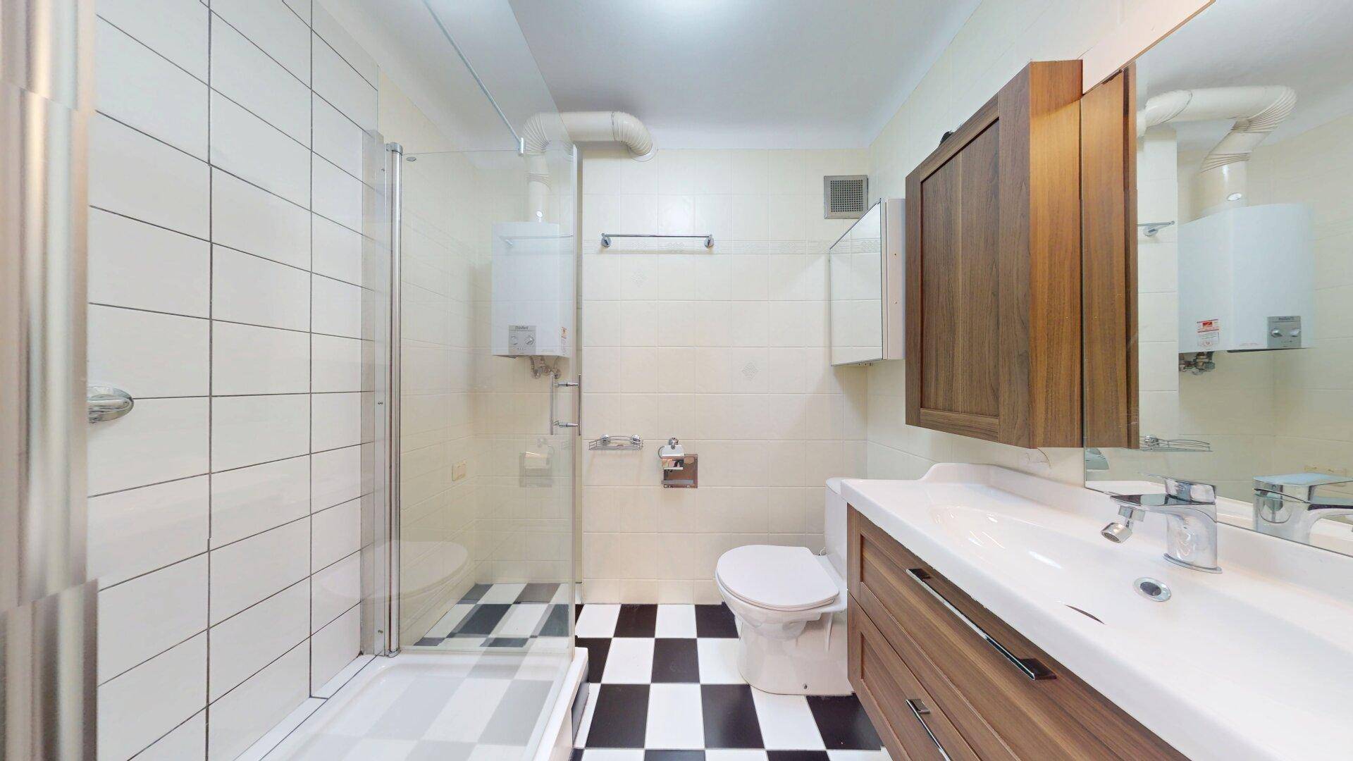 Badezimmer mit Duschkabine, WC und Waschbecken, ausgestattet mit markanten schwarz-weißen Fliesen.
