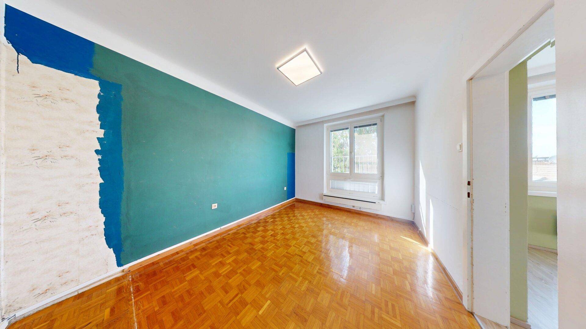 Schlafzimmer mit Parkettboden und farbiger Wandgestaltung, das viel Tageslicht hereinlässt.
