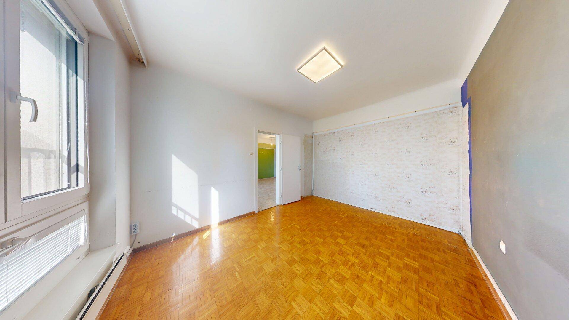 Schlafzimmer mit Parkettboden und großem Fenster, das viel Tageslicht hereinlässt.