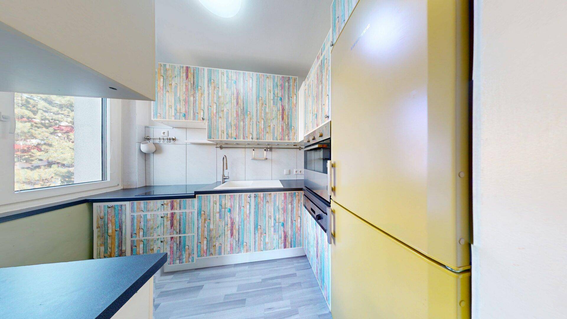 Helle Küche mit bunten Schrankfronten, Fenster und integriertem Kühlschrank und Backofen.
