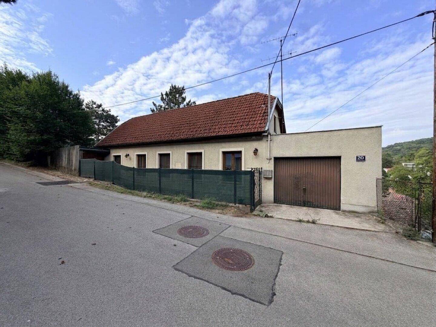 Älteres Haus mit Ziegeldach und beige Fassade, direkt an der Straße gelegen mit integrierter Garage.
