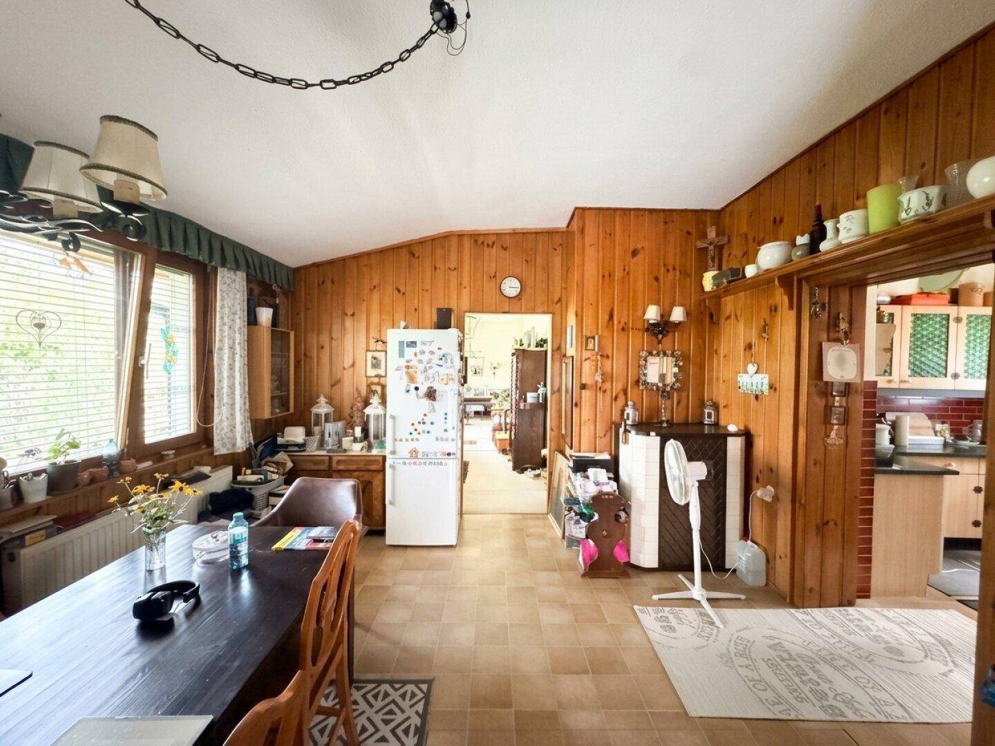 Rustikaler Wohn- und Essbereich mit Holzwänden, Fliesenboden und einem großen Esstisch.