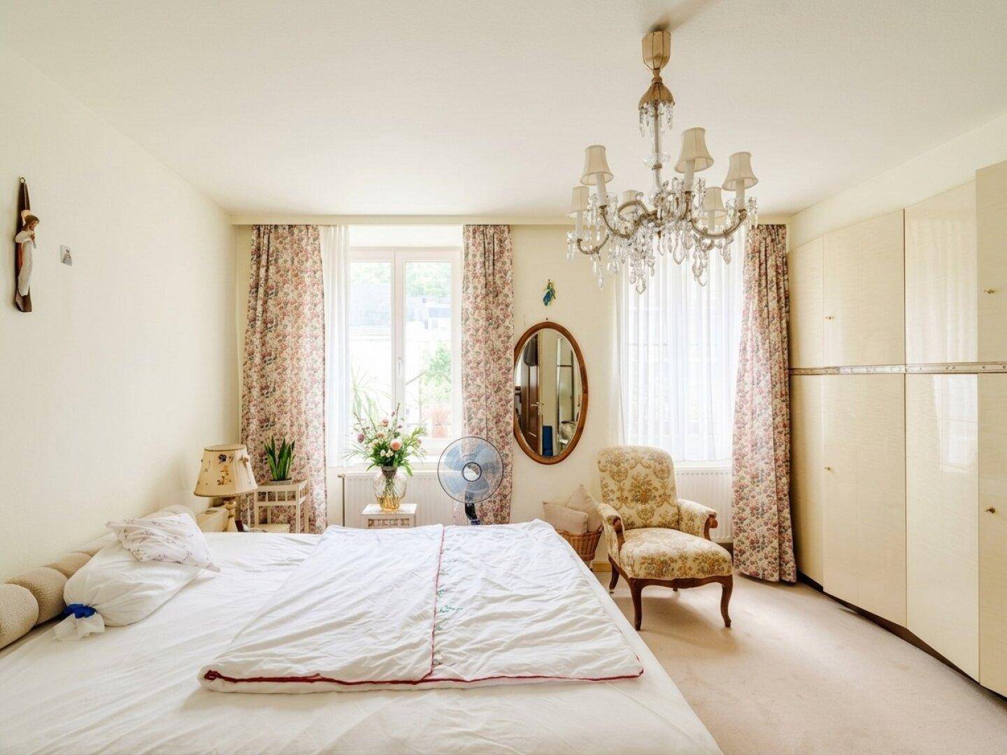 Helles Schlafzimmer mit großem Bett, Kronleuchter, floralen Vorhängen und einem geräumigen Kleiderschrank.