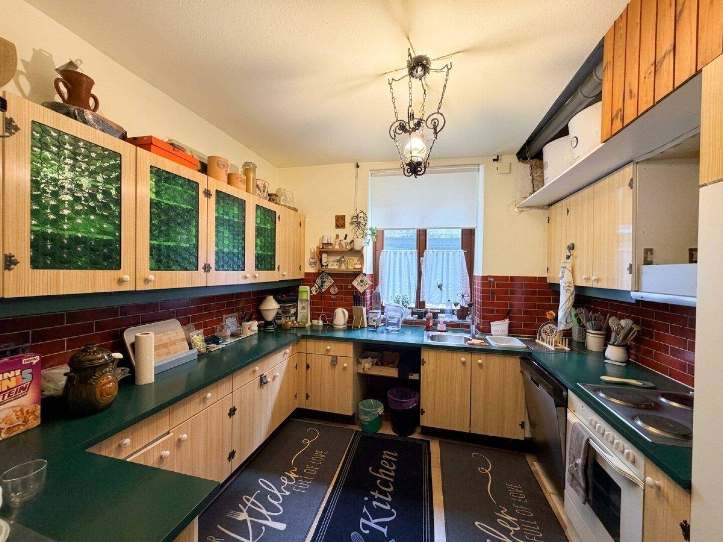Traditionelle Küche mit grünen Arbeitsplatten, roten Fliesen und Holzschränken mit grünen Glaseinsätzen.