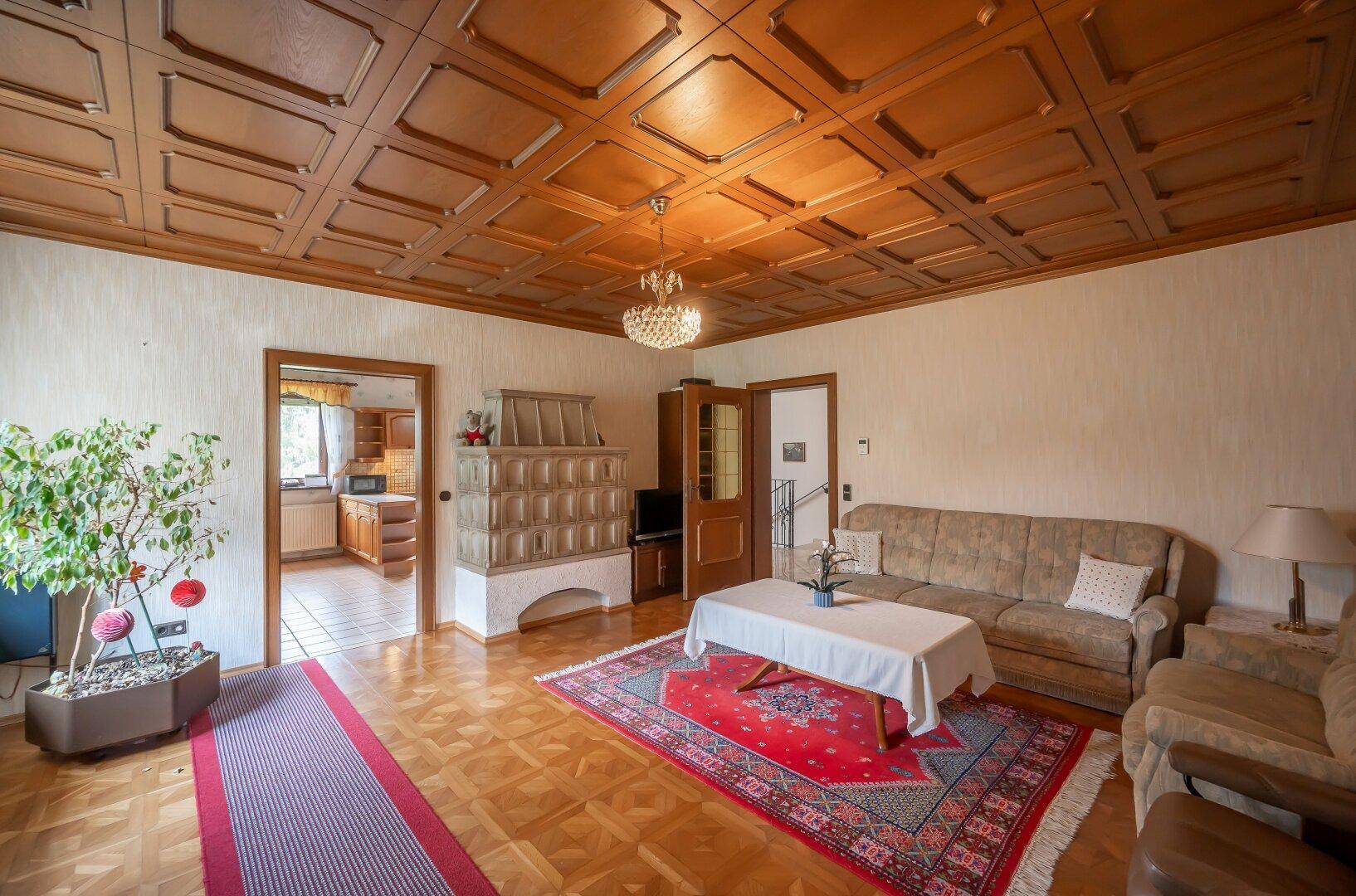 Traditionelles Wohnzimmer mit Parkettboden, Holzkassettendecke, bequemen Sofas und einem Kachelofen.