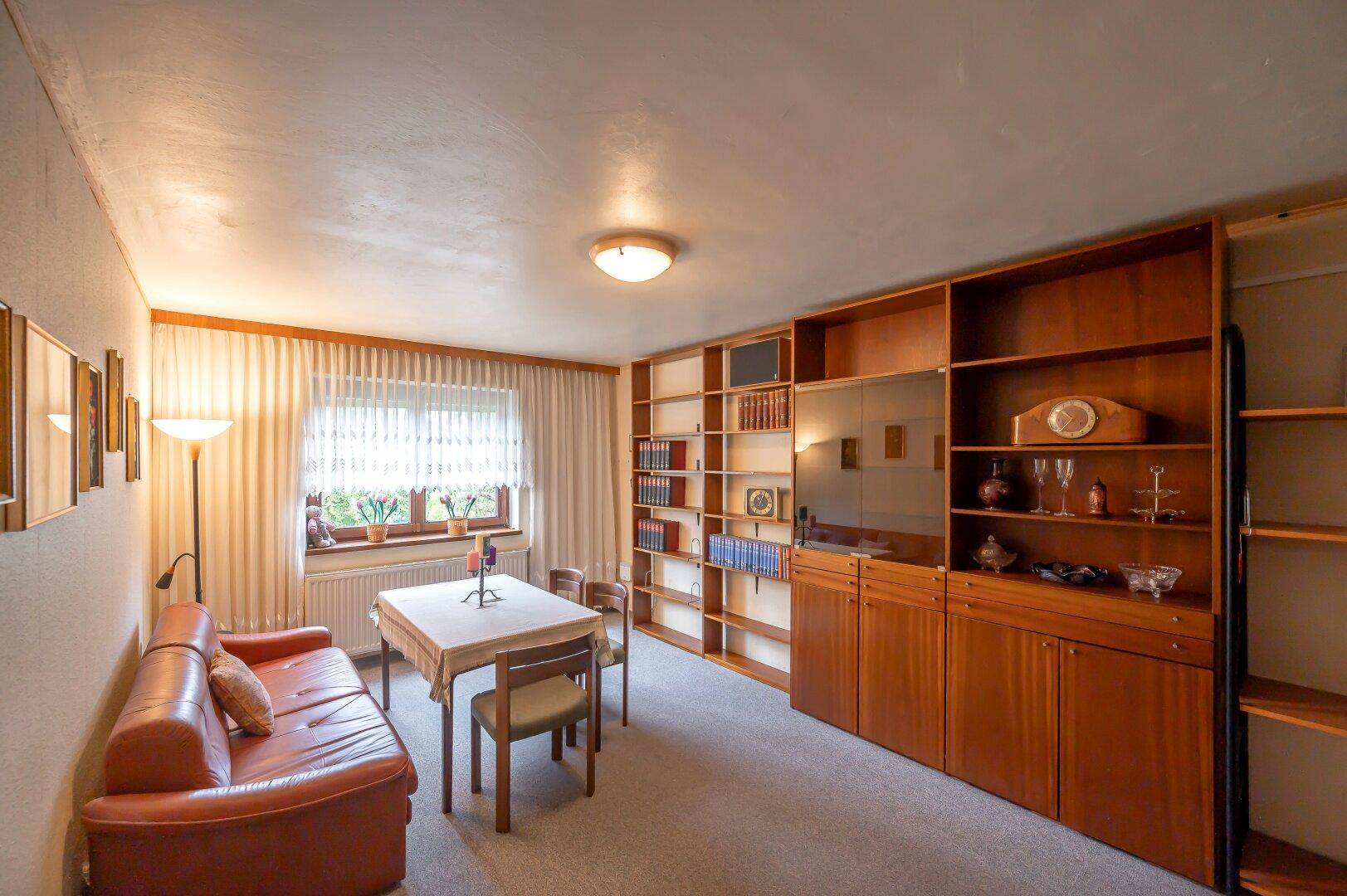 Arbeitszimmer mit Teppichboden, großer Bücherwand, Ledersofa und einem Fenster für natürliches Licht.