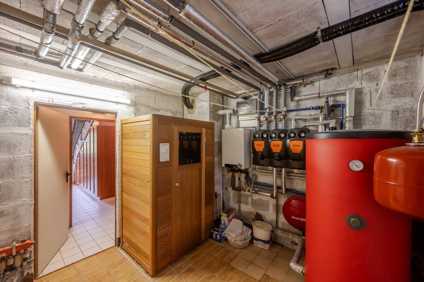 Kellerraum mit einer Sauna, Heizungsanlagen und sichtbaren Rohrleitungen.