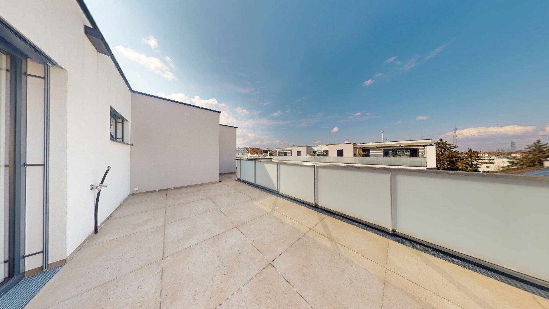 Große, sonnige Dachterrasse mit Fliesenboden und Glasgeländer, bietet einen weiten Blick.