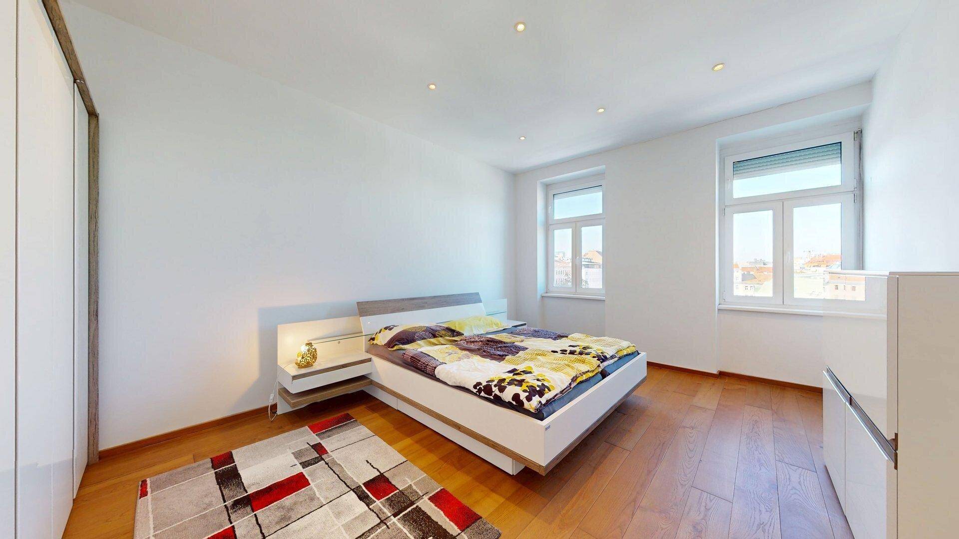 Schlafzimmer mit Holzboden, großem Bett, Einbauschrank und viel Tageslicht.