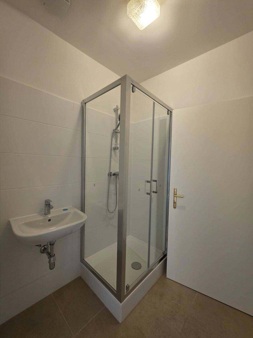 Modernes Badezimmer mit Duschkabine, Waschbecken und hellen Fliesen.
