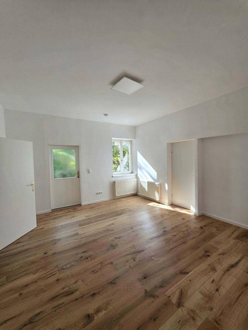 Geräumiger, heller Raum mit Holzboden und einem Fenster, das viel Sonnenlicht hereinlässt.