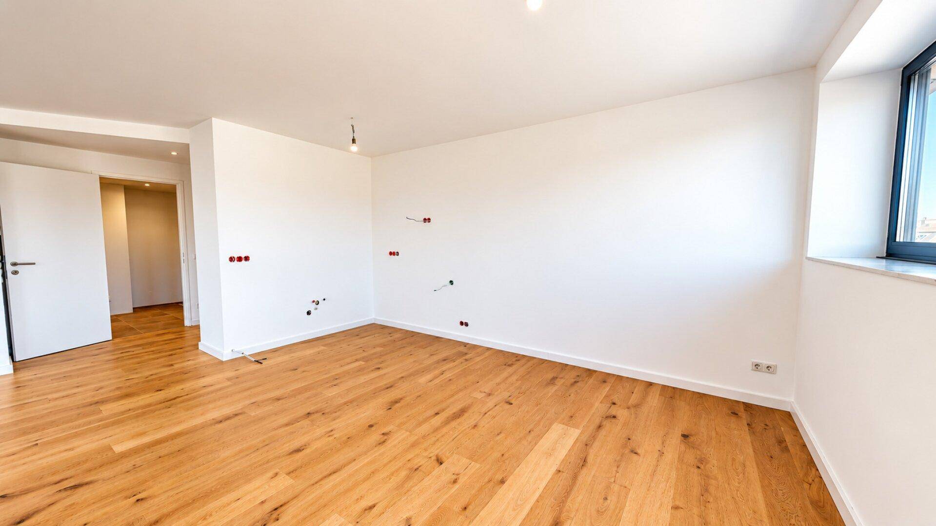 Leerer Wohnraum mit Holzboden und weißen Wänden, vorbereitet für Elektroinstallationen.